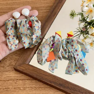 Close-up detail of chiffon fabric bow earrings with shell studs and colorful charms
