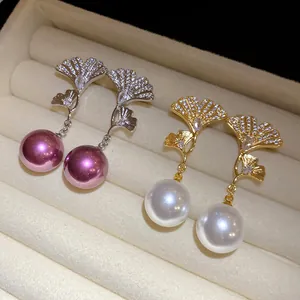 Close-up of elegant ginkgo leaf pearl drop earrings showcased in a luxury beige jewelry box
