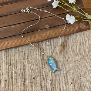 Detailed view of an iridescent blue fish pendant necklace on a rustic burlap surface