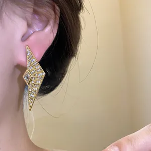 Close-up of geometric gold rhombus stud earrings with sparkling zircon stones and silver needle