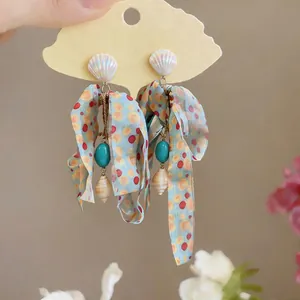 Macro detail of nautical style earrings featuring seashells and colorful chiffon ribbons