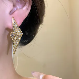 Detail close-up of geometric gold zircon stud earrings shown worn on a model's ear