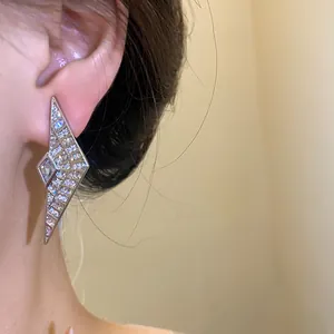 Close-up view of geometric silver earrings with sparkling zircon stones on an ear.