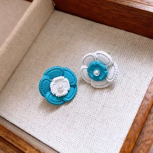 Primo piano di orecchini a lobo a fiore blu e bianchi con eleganti perle centrali