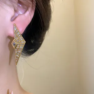 Macro view of a geometric gold-toned zircon earring worn on a model's ear for detail