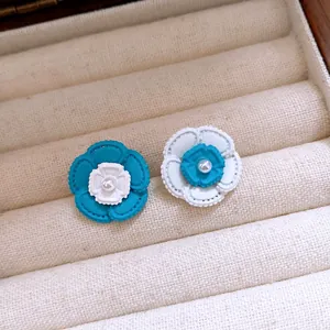 Dettaglio degli orecchini a lobo a camelia blu e bianchi con perla centrale.