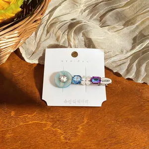 Close-up of elegant hair clip featuring colorful resin, crystals, and a Lucky charm tag