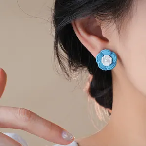 Primo piano di un orecchino a fiore blu con perla bianca indossato sull'orecchio.