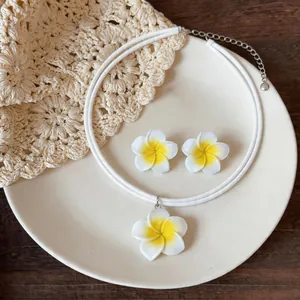Vue détaillée d'une parure de bijoux fleur de frangipanier en résine blanche, collier et boucles.