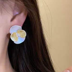 Close-up view of an elegant enamel flower stud earring with a central pearl shown on the ear