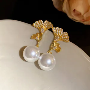 Elegant close-up of gold ginkgo leaf earrings with white pearl drops and zircon accents.