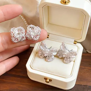 Close-up of elegant hollow lace and butterfly pearl stud earrings in a white gift box