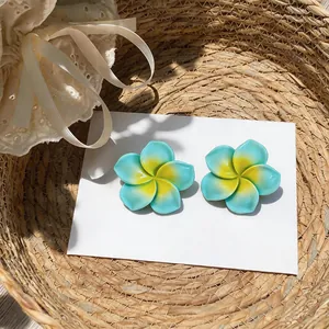 Gros plan de boucles d'oreilles fleurs en résine bleue et jaune élégantes sur carte blanche.