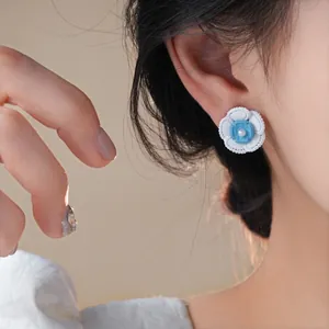 Dettaglio dell'orecchino a fiore blu e bianco con perla centrale all'orecchio
