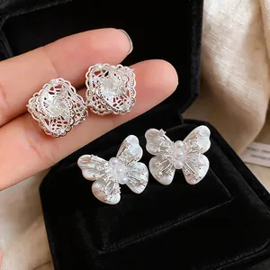Detailed shot of hollow lace diamond studs and butterfly pearl earrings in a black box
