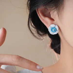 Dettaglio dell'orecchino a fiore bianco e blu con perla sull'orecchio della modella