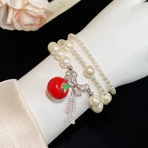 Pulsera de perlas de varias capas con dije de manzana roja y lazo de circón brillante.