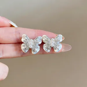Close-up of butterfly stud earrings with shell wings, pearls, and sparkling zircons.