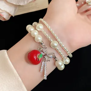 Vista detallada de una pulsera de perlas multicapa con dije de manzana roja y lazo