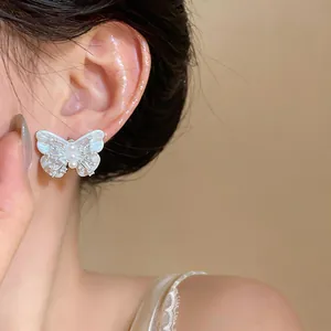 Close-up of an elegant pearlescent butterfly earring with zircon details on a woman's ear.