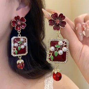 Close-up of retro red floral drop earrings with pearls and crystal details held by hand.