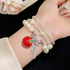 Primer plano de pulsera de perlas multicapa con dije de manzana roja y lazo brillante