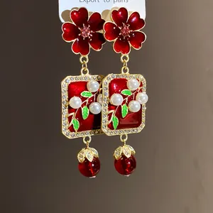 Close-up detail showing red enamel flower and pearl drop earrings in vintage style