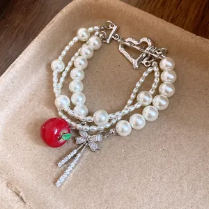 Primer plano de una pulsera de perlas multicapa con un dije de manzana y lazo de circón.