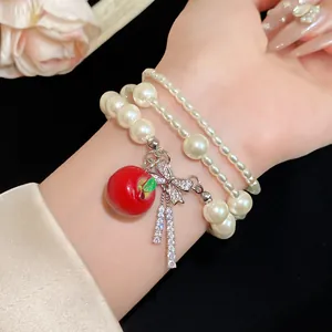 Vista detallada de pulsera de perlas multicapa con lazo de circón y dije de manzana