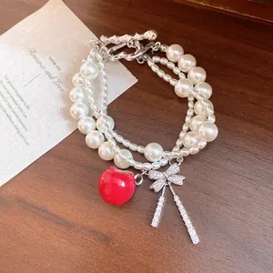 Primer plano de una pulsera de perlas multicapa con dije de manzana roja y lazo de circón.