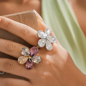 Detailed close-up of two sparkling crystal flower rings with purple and clear petals on a hand.