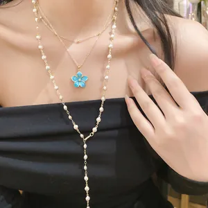 Close-up detail of a layered gold necklace featuring a blue flower and pearls