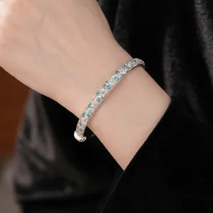 Elegant silver-tone bangle set with green and clear cubic zirconia worn on wrist