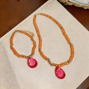 Parure de bijoux en perles oranges avec pendentifs en forme de goutte rose : collier et bracelet