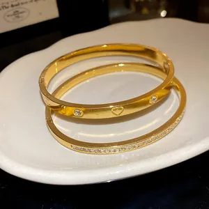 Close-up of gold stainless steel bangles with heart and zircon accents on a white plate.