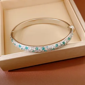 Close-up detail of an elegant silver bangle set with white and teal pavé cubic zirconia