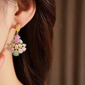 Elegant detail of multi-colored teardrop fan-shaped gold earrings being worn on an ear.