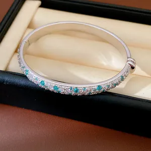 Detailed macro shot of a silver geometric bangle with teal and clear zircon in a gift box