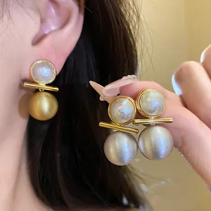 Detail of 18k gold plated brushed metallic and pearl round stud earrings on ear