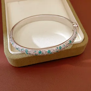 Close-up of silver bangle with teal and white cubic zirconia stones in box.