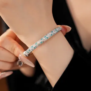 Detailed close-up of a sparkling turquoise and white zircon paved bangle worn on wrist