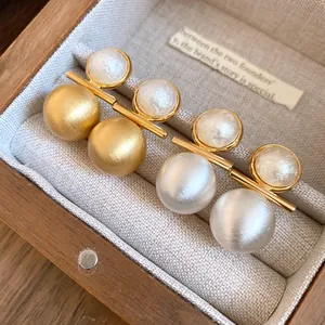 Detailed macro view of 18k gold plated brushed stud earrings featuring elegant pearls