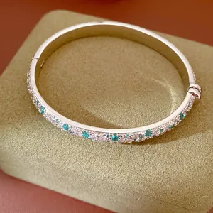 Close-up of silver-tone bangle with inlaid turquoise and clear stones on jewelry box.