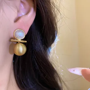 Detailed close-up of 18k gold plated brushed spherical earrings featuring shell inlay detail