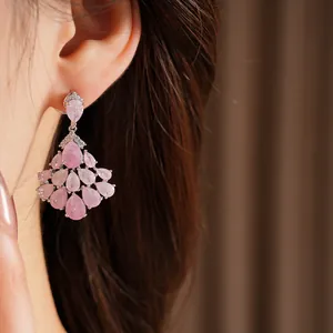 Detail view of 14k gold plated fan-shaped tassel earrings with pink teardrop stones.