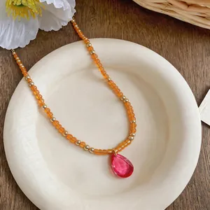 Vue détaillée d'un collier de perles avec pendentif goutte rose sur une assiette