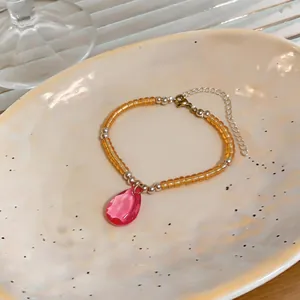Gros plan d'un bracelet en perles avec un pendentif goutte d'eau en cristal rose.
