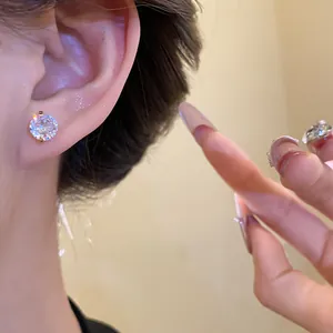 Close-up of sparkling zirconia stud earring worn on ear with manicured hand