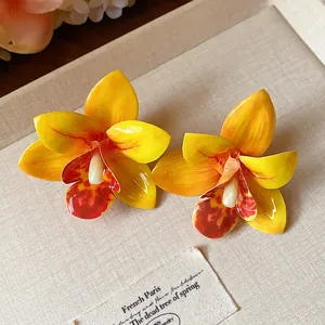 Nahaufnahme gelber Orchideen-Resin-Ohrstecker mit Hochglanzfinish und Silberstiften