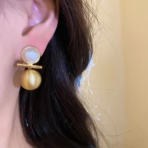Detailed view of 18k gold plated brushed ball earring with opalescent stone worn on ear